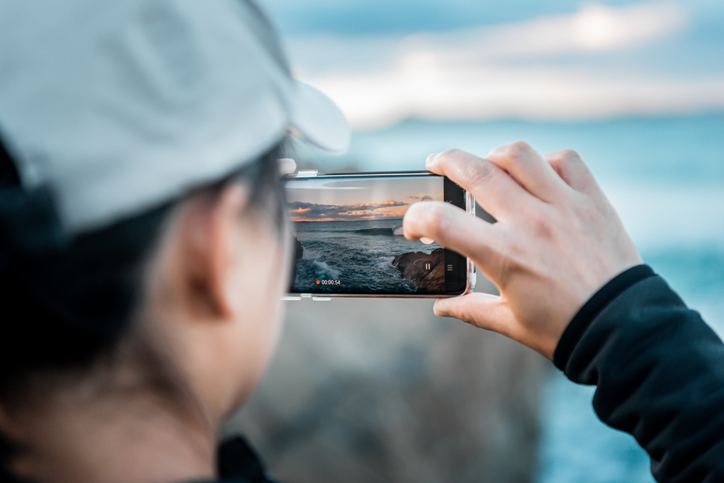 Person captures ocean sunset on smartphone, SociShare, Social Media Management